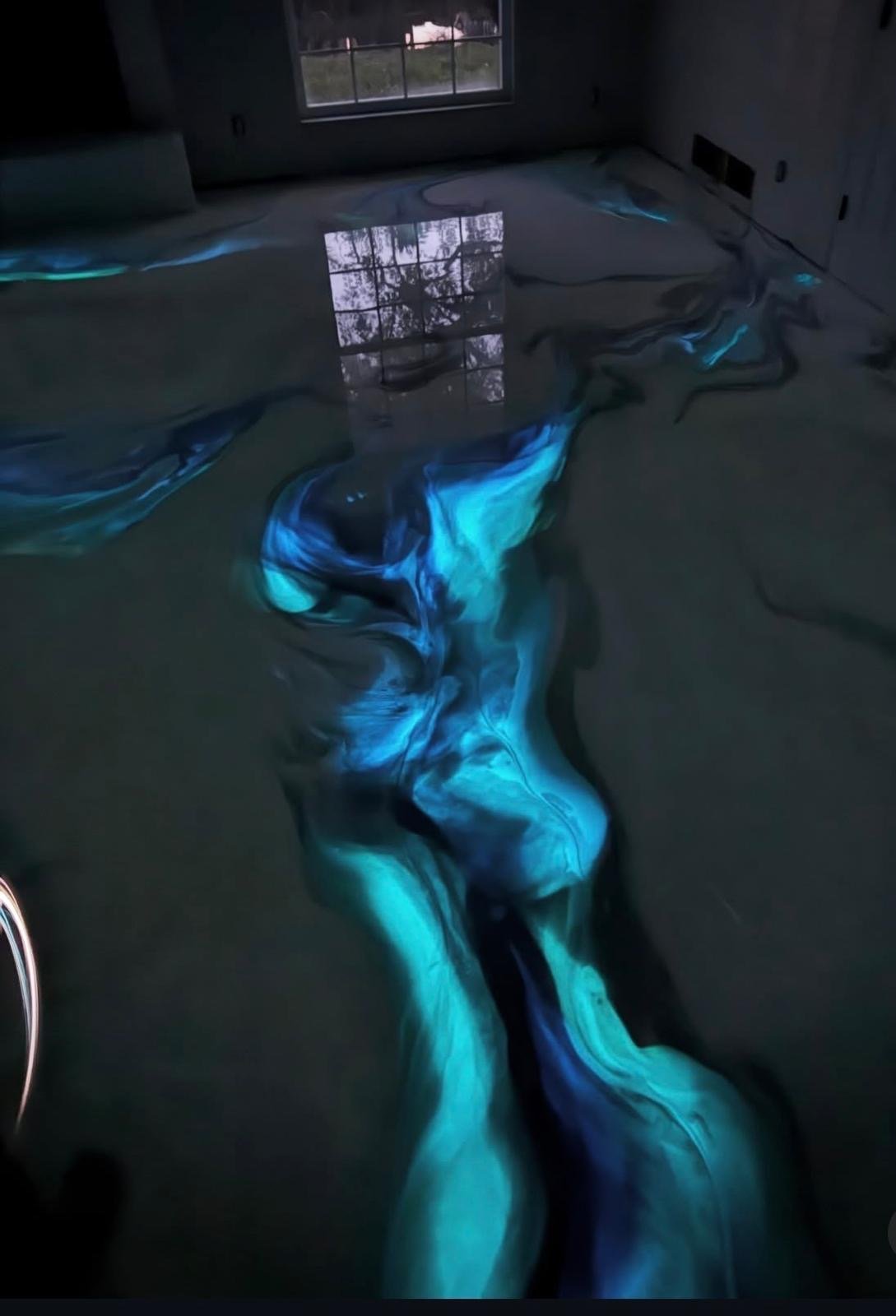 Glowing blue neon light projection on floor of empty room with window and video screen displaying cityscape