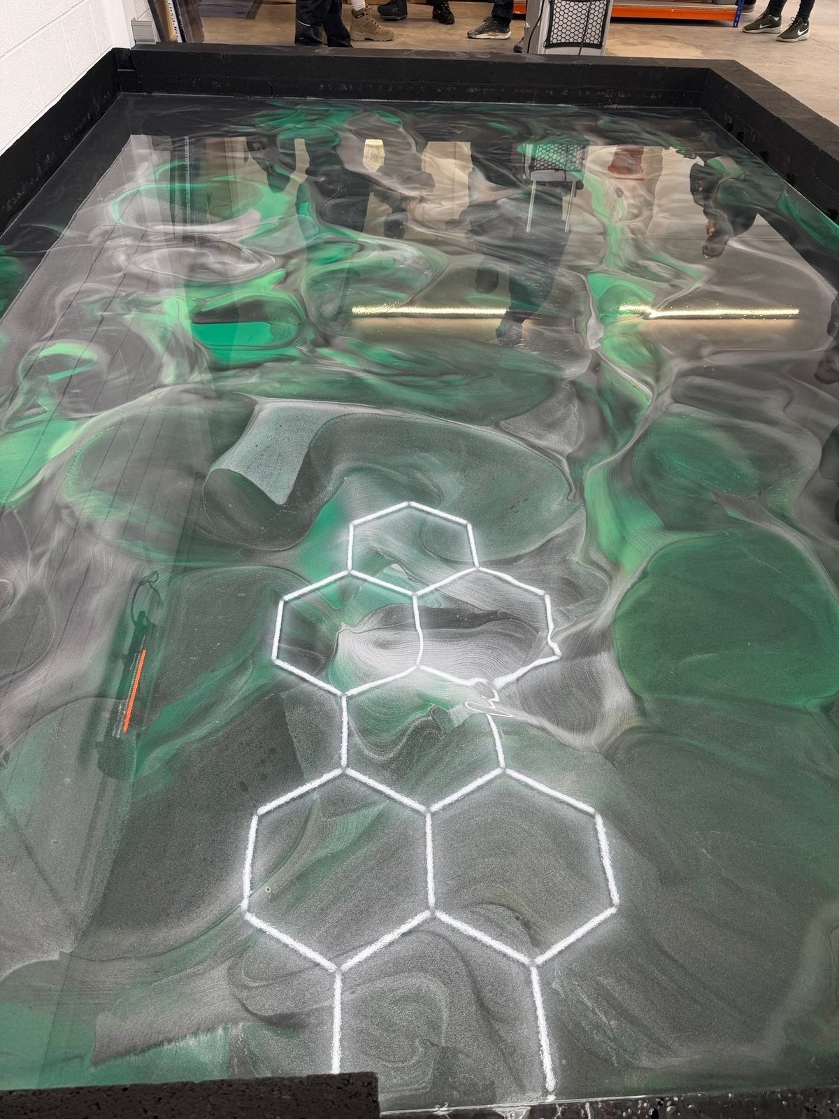 Interactive floor display with glowing white hexagon pattern and green laser lights overlaid on a textured surface